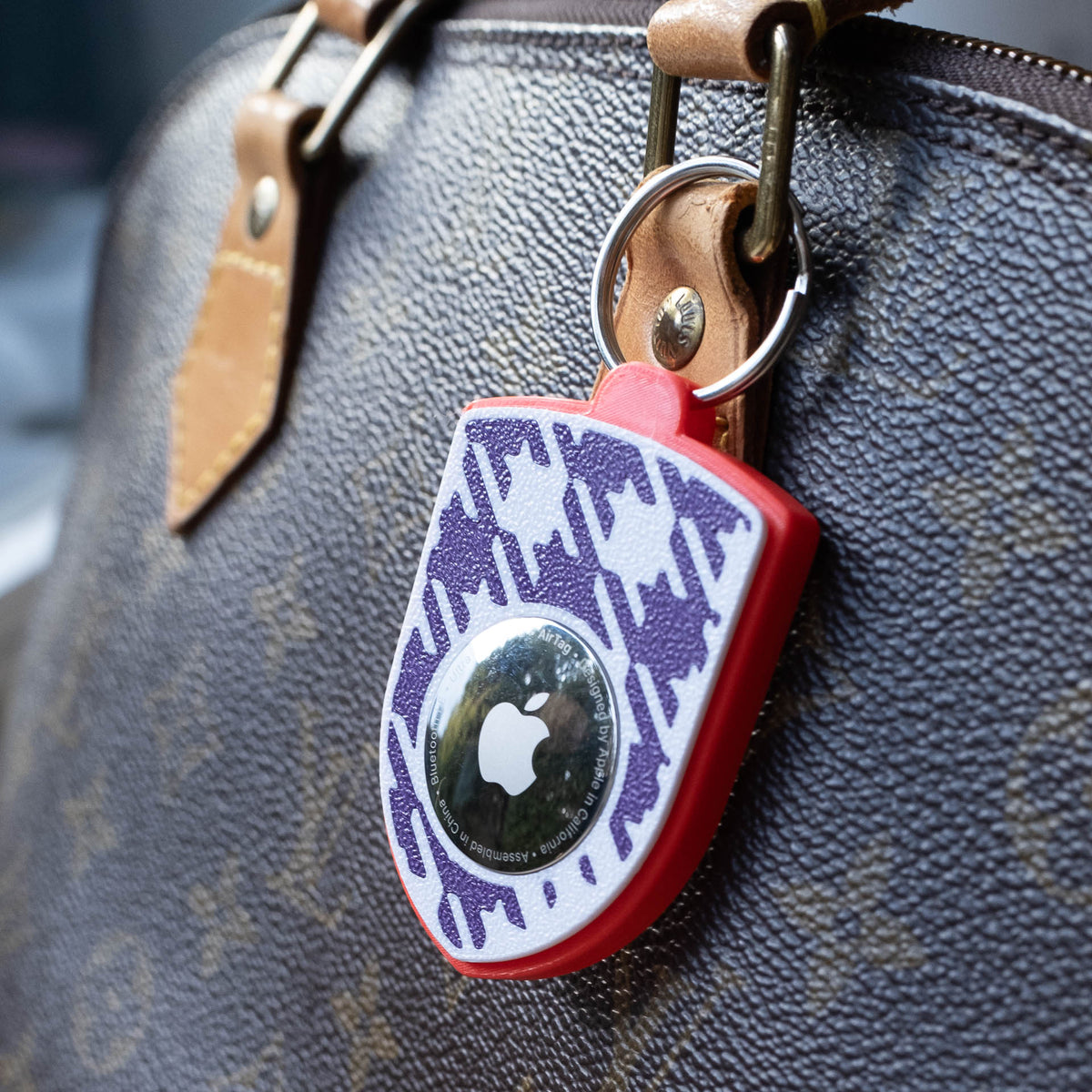 Rot-violetter AirTag-Schlüsselanhänger mit Pepita an einer Handtasche