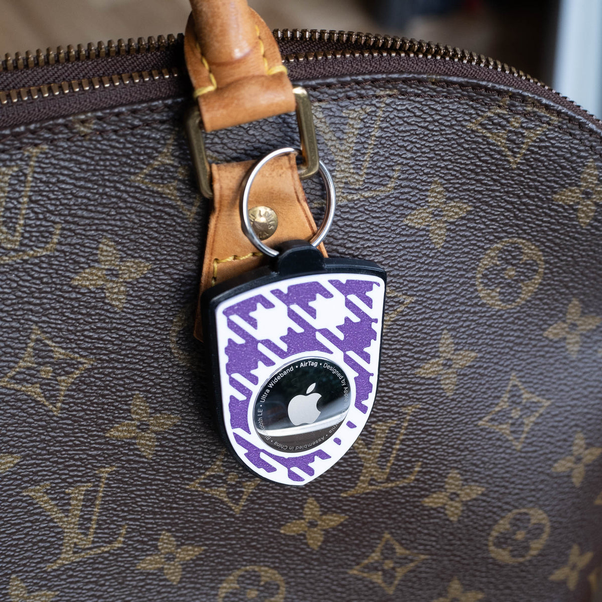 Schwarz-violetter AirTag-Schlüsselanhänger mit Pepita an einer Handtasche