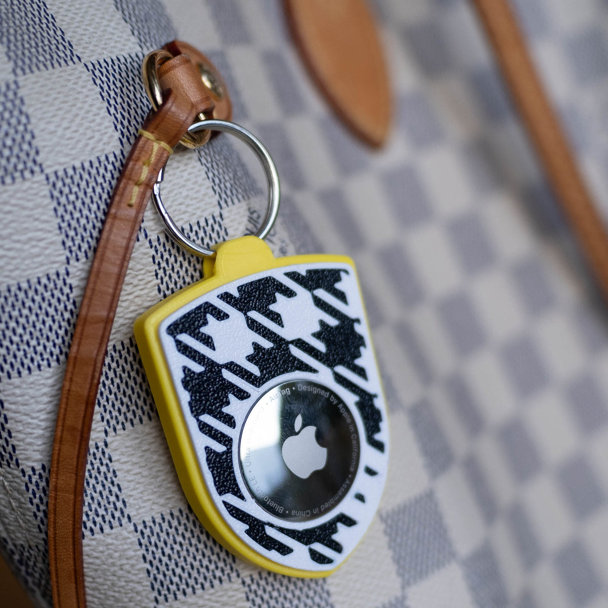 Gelb-schwarzer AirTag-Schlüsselanhänger mit Pepita an einer Handtasche