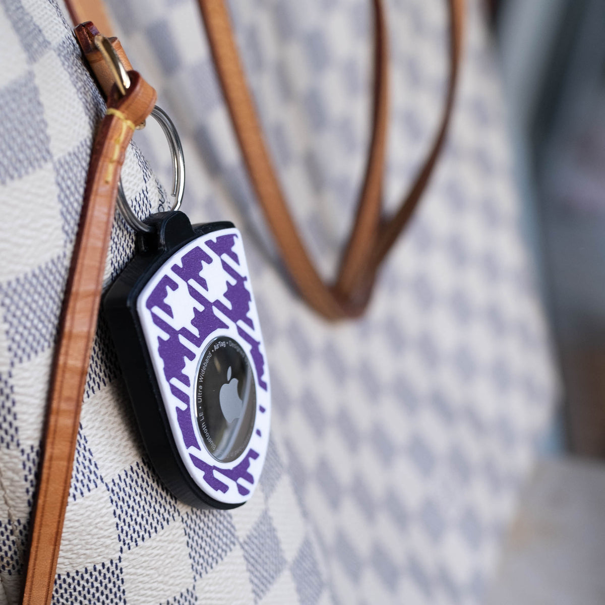 Schwarz-violetter AirTag-Schlüsselanhänger mit Pepita seitlich an einer Handtasche