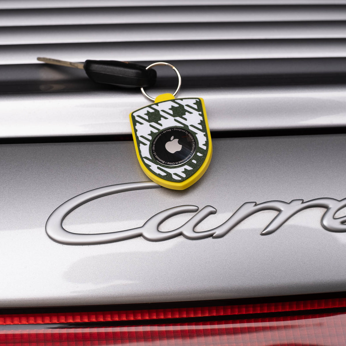 Gelber AirTag-Schlüsselanhänger mit grün-weißem Pepita am Porsche Carrera